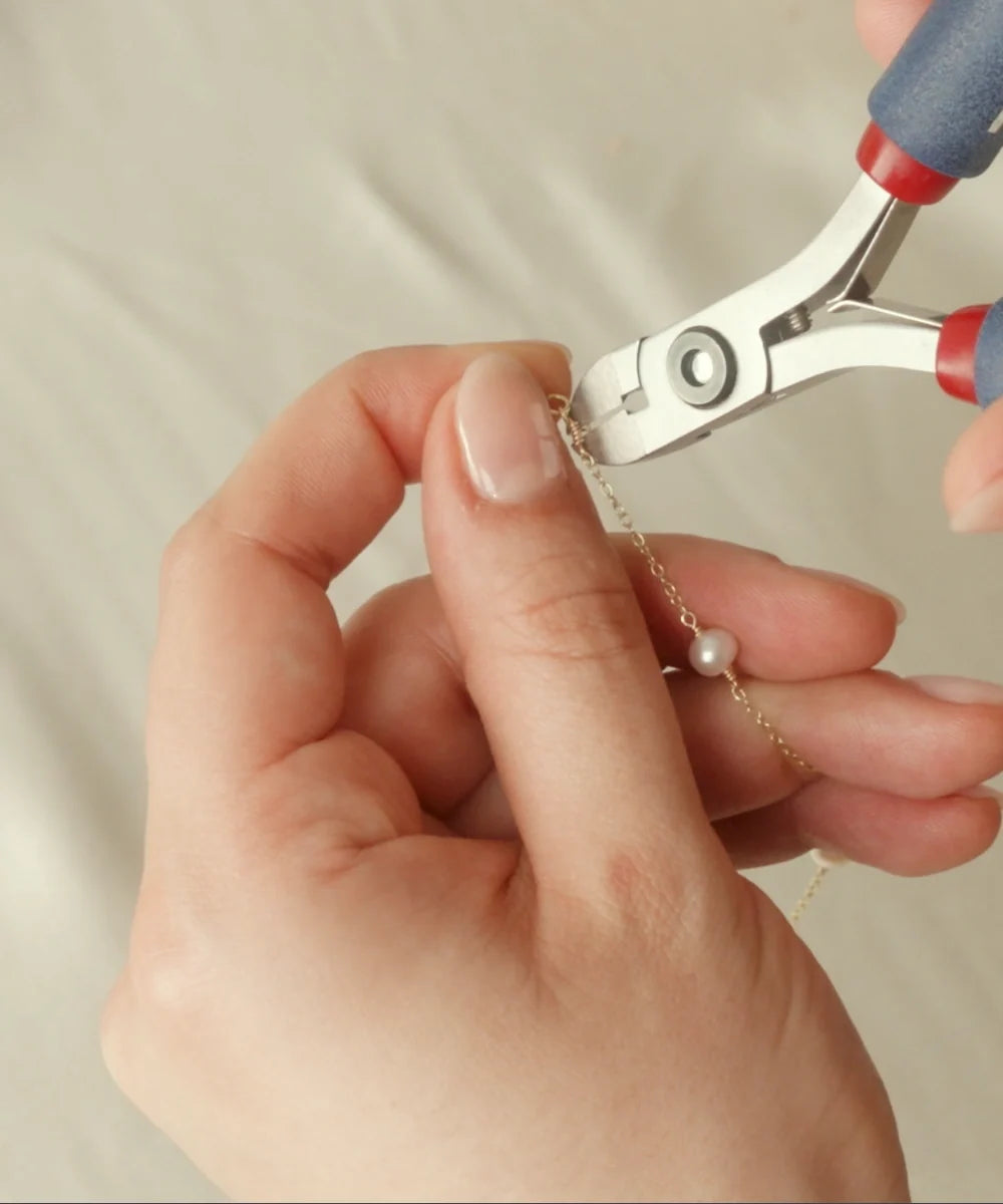 Close-up of a LILY & ROO team member handcrafting a delicate pearl necklace using jewellery pliers in our London studio.