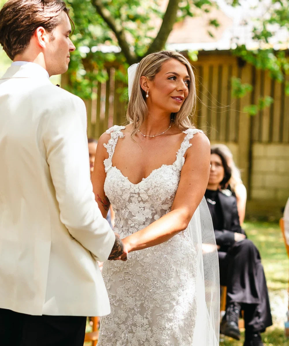 Bride and groom holding hands during their outdoor wedding ceremony, with the bride wearing pearl drop earrings and a delicate pearl necklace.