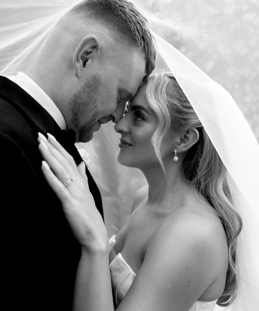 bride wearing silver huggie pearl drop earrings, forehead to forehead with groom under her veil at foxtail barns wedding