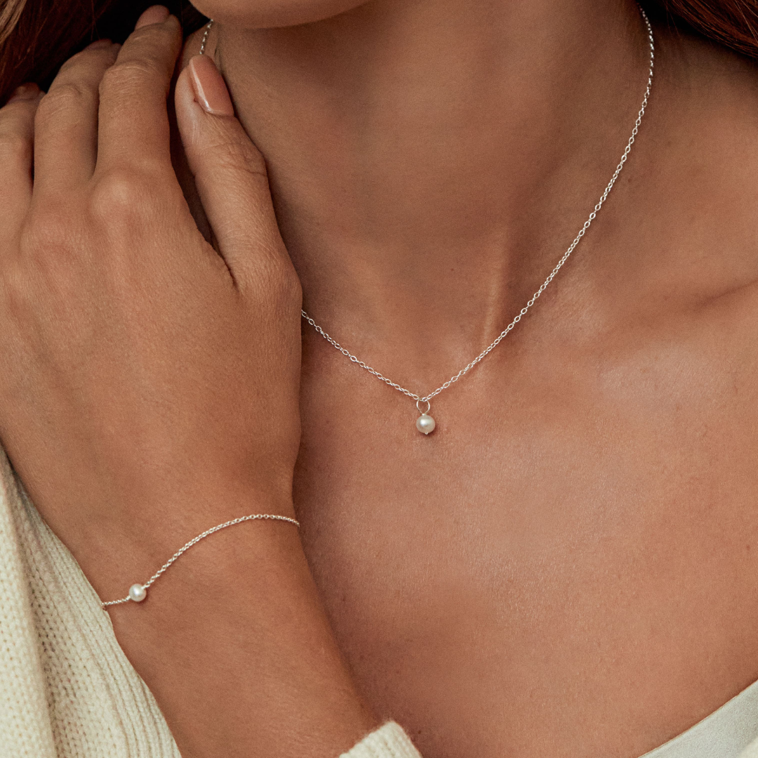Woman wearing a silver single pearl bracelet on her wrist and silver single pearl choker around her neck