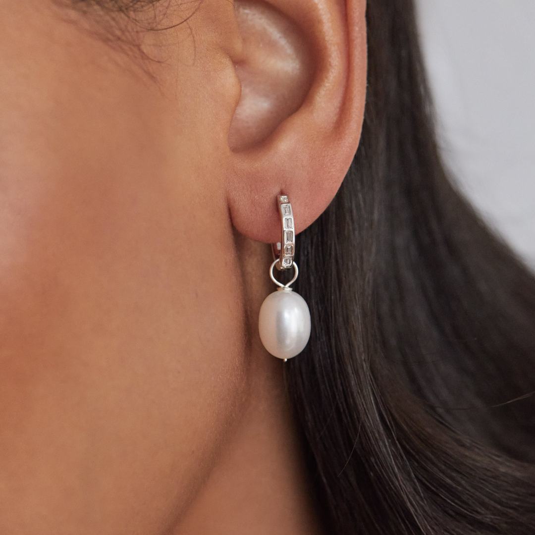 Silver diamond style baguette pearl drop hoop earring in one ear lobe close up