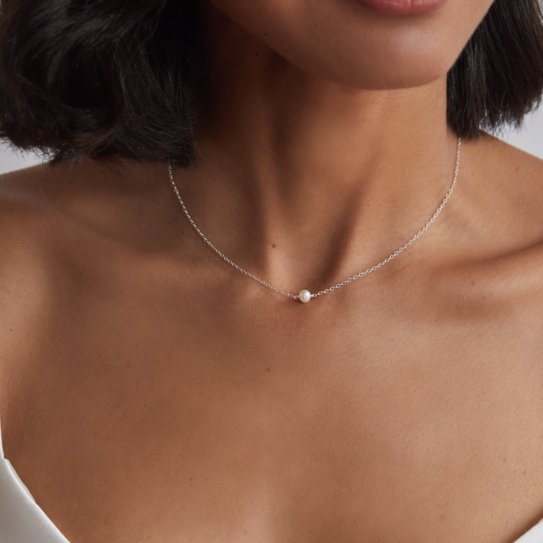 Close up of a woman with a bob haircut wearing a silver single pearl choker around her neck