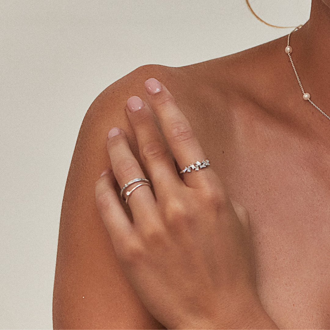 Silver thin diamond style stacking ring on a finger stacked with another silver ring and a silver diamond style baguette ring on another finger