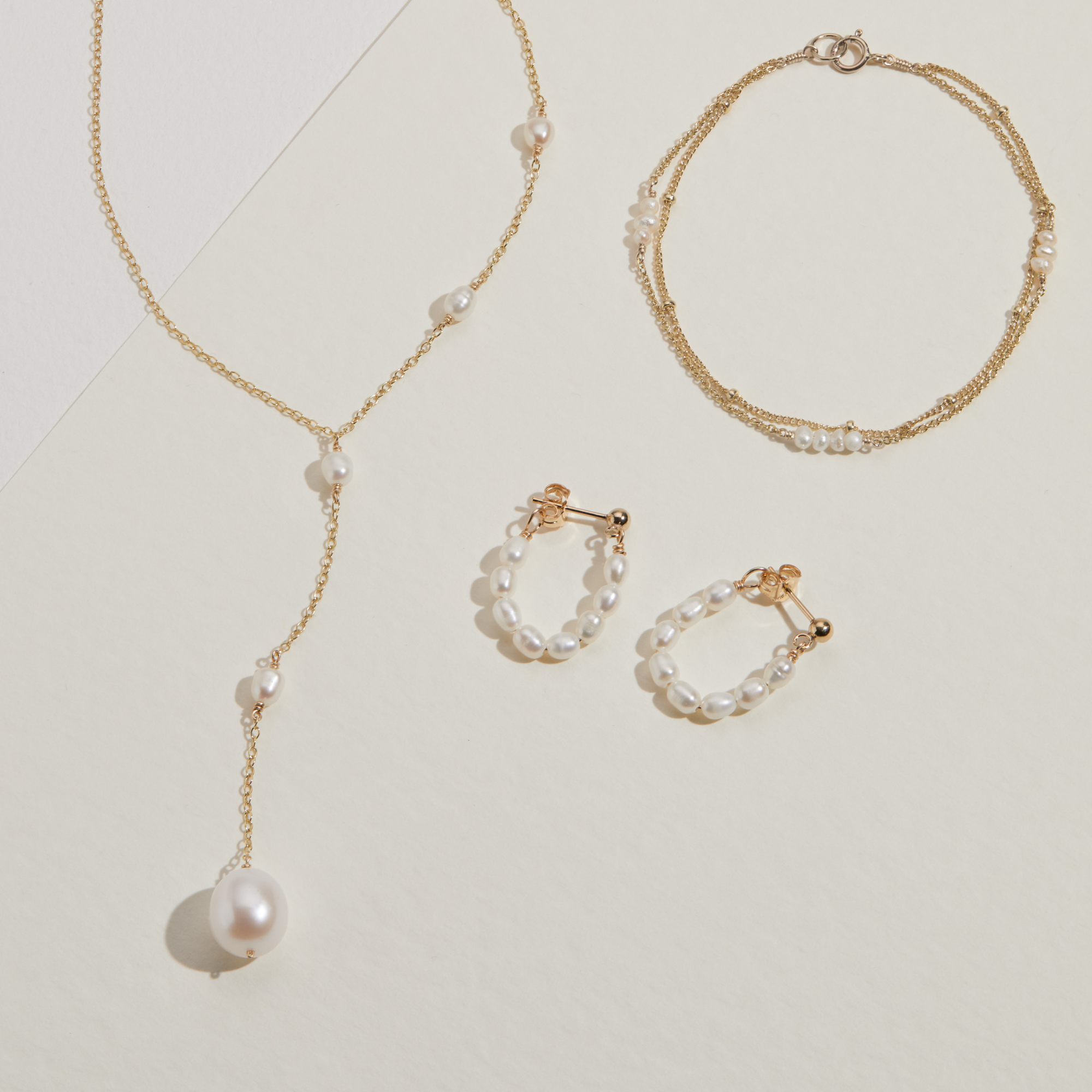 Gold seed pearl hoop earrings, a gold cluster bracelet and a gold seed pearl lariat necklace on a paper surface