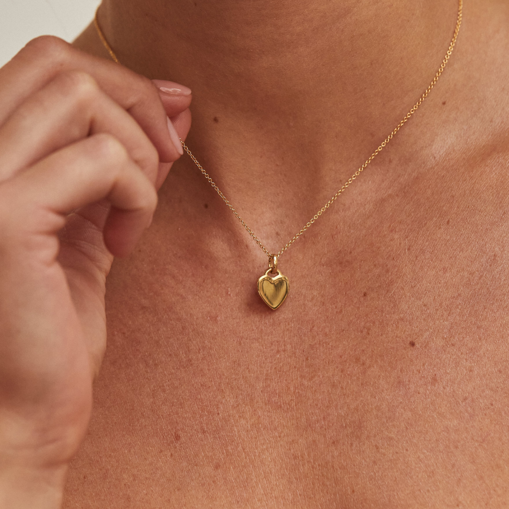 Gold heart padlock pendant necklace with an engraved border around a neck with fingers clasping the chain