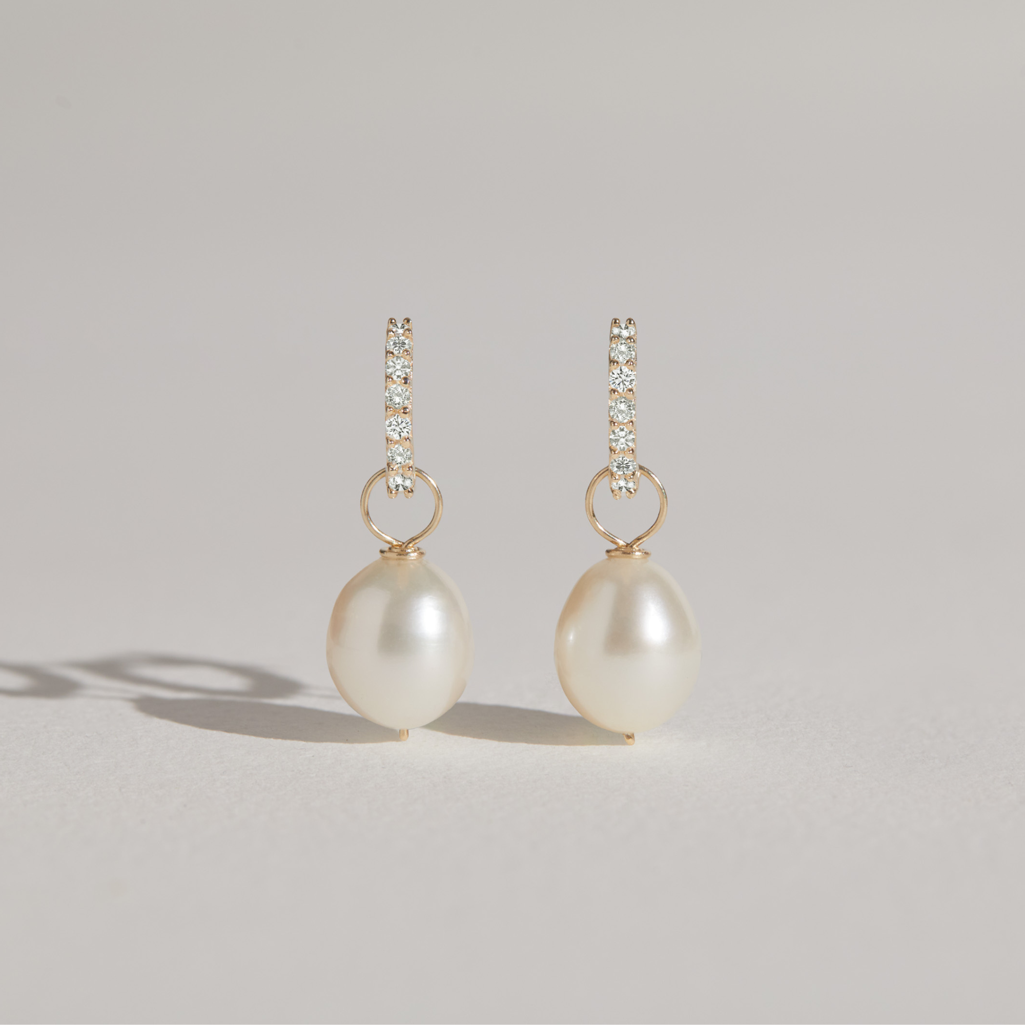 Gold huggie pearl drop earrings on a grey background with shadows