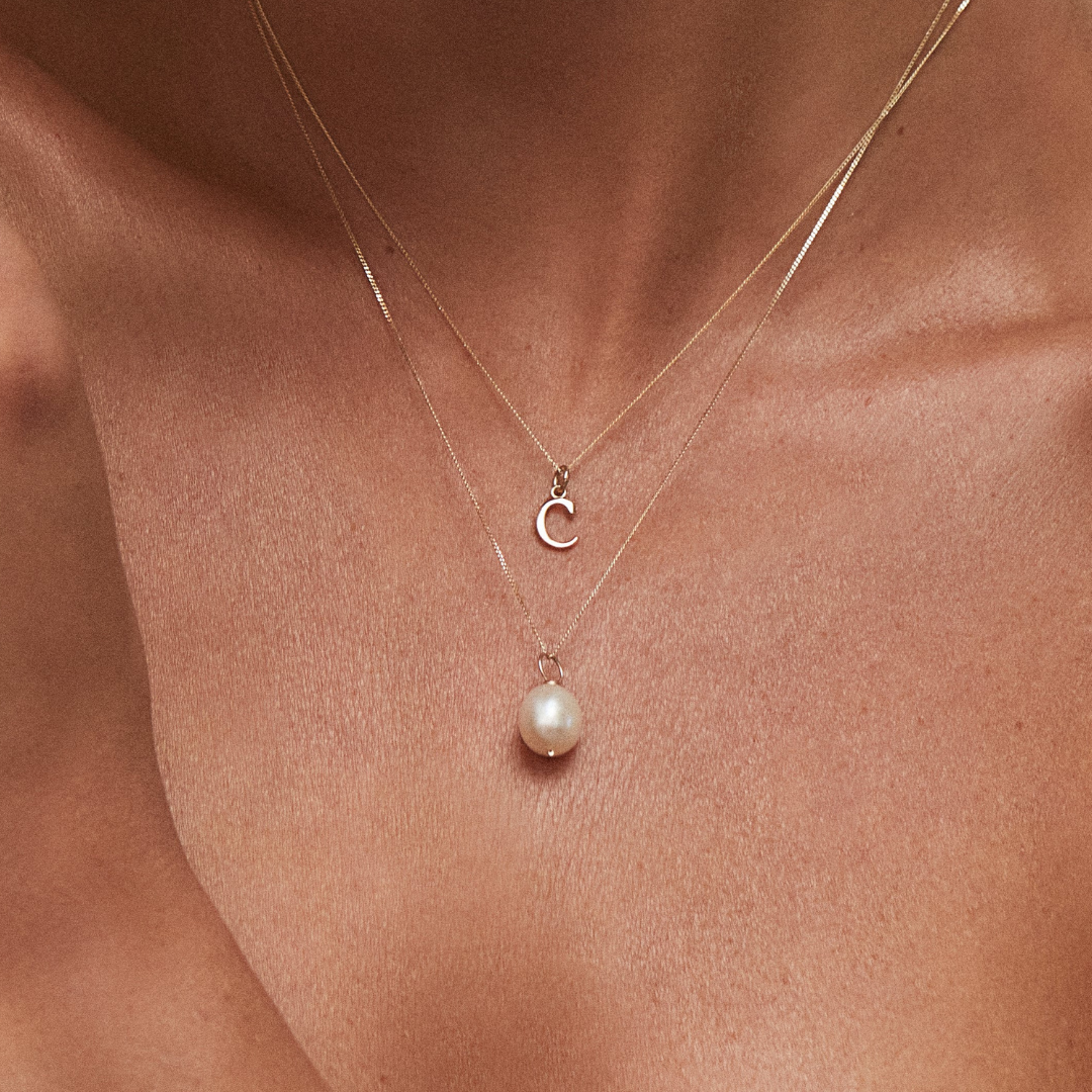 Solid gold curve initial letter necklace 'C' and a gold single pearl necklace around a neck