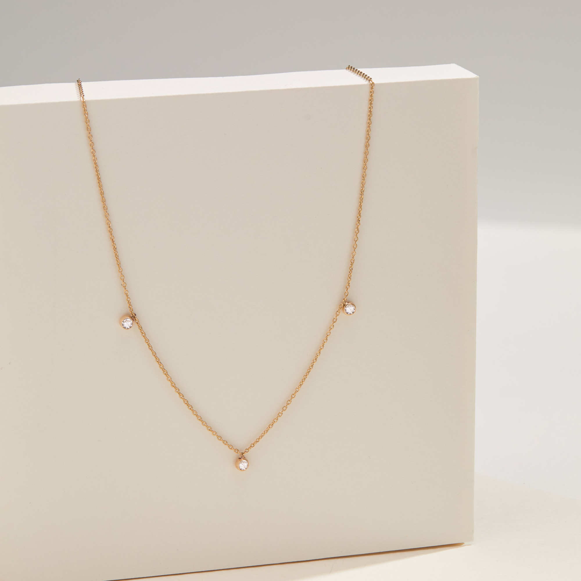 Solid gold diamond drop necklace hanging over a solid white block