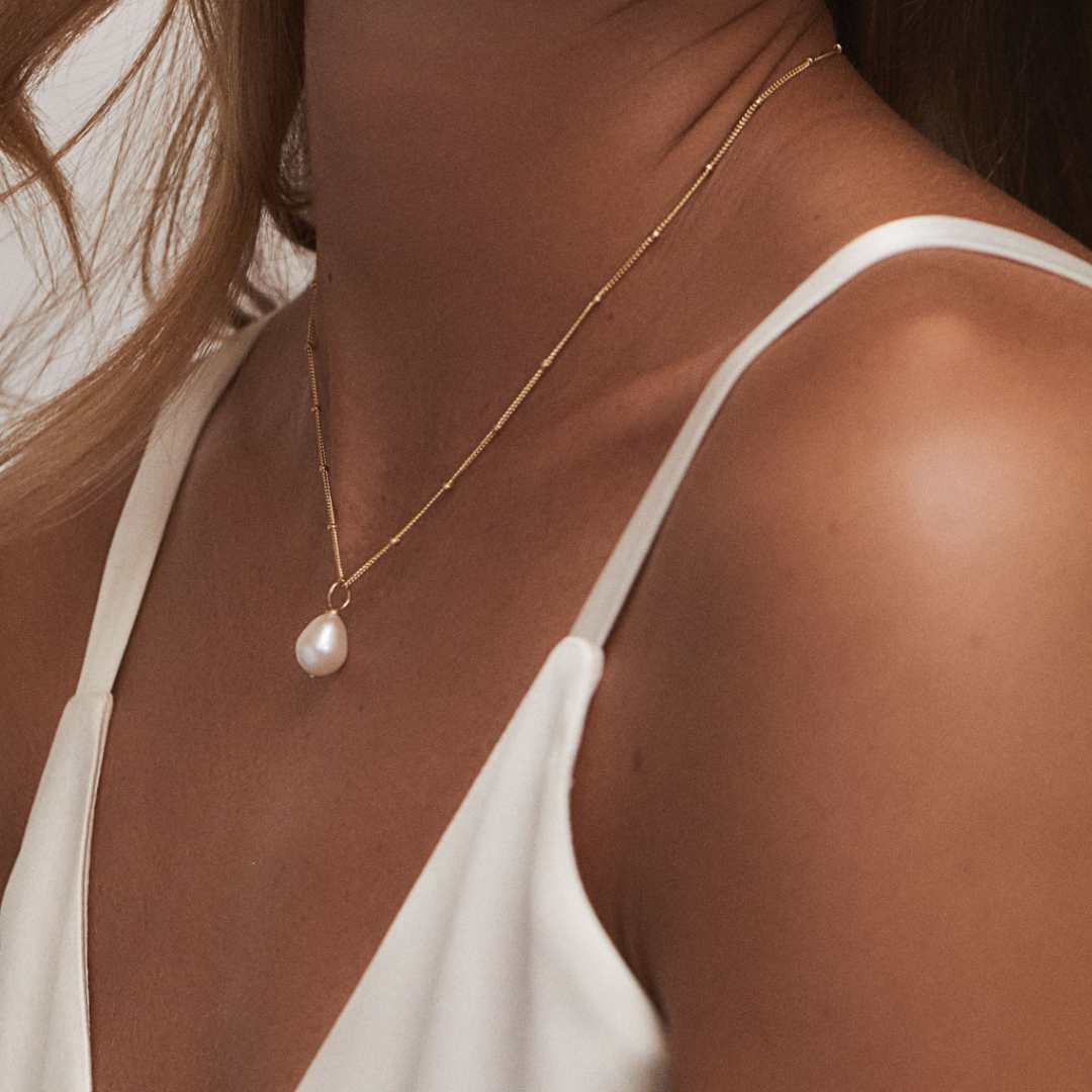 Side angle of a gold large pearl satellite necklace around a neck with a white top