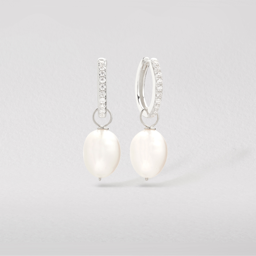 A silver diamond style large pearl drop hoop earrings over paper backdrop