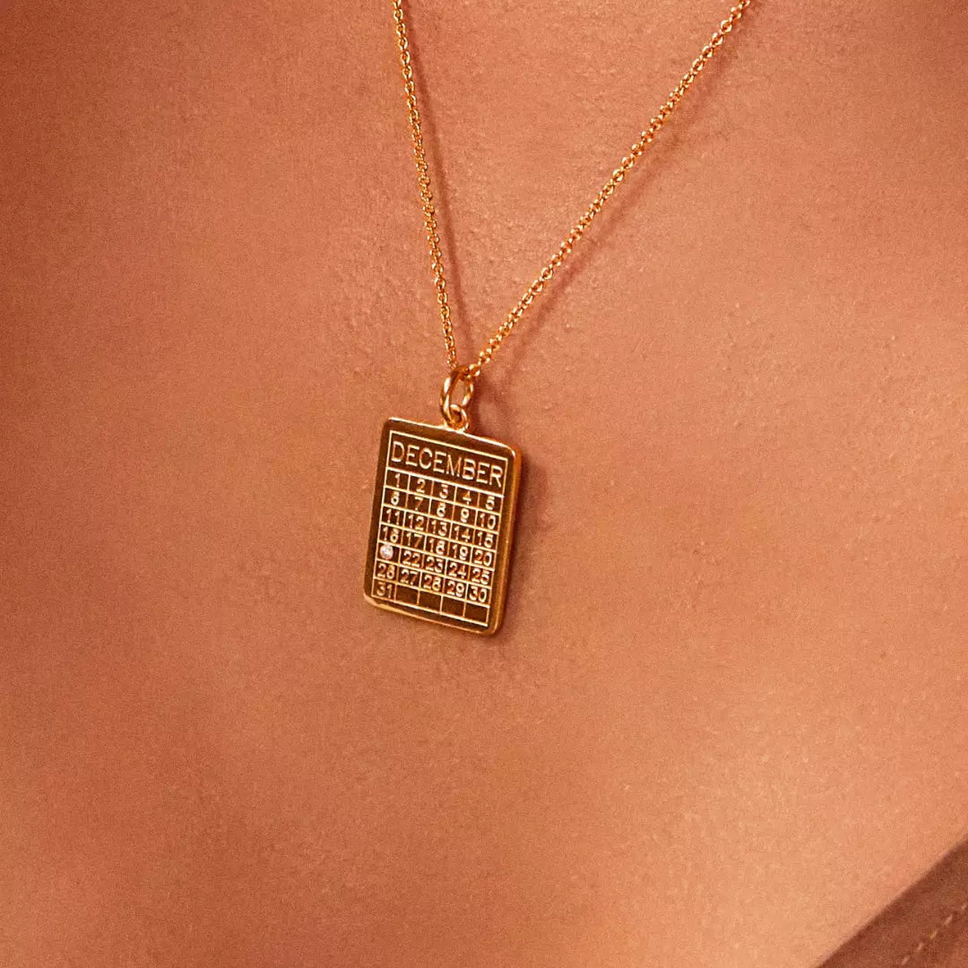 Gold special date calendar necklace with a gemstone on December 21st around a neck