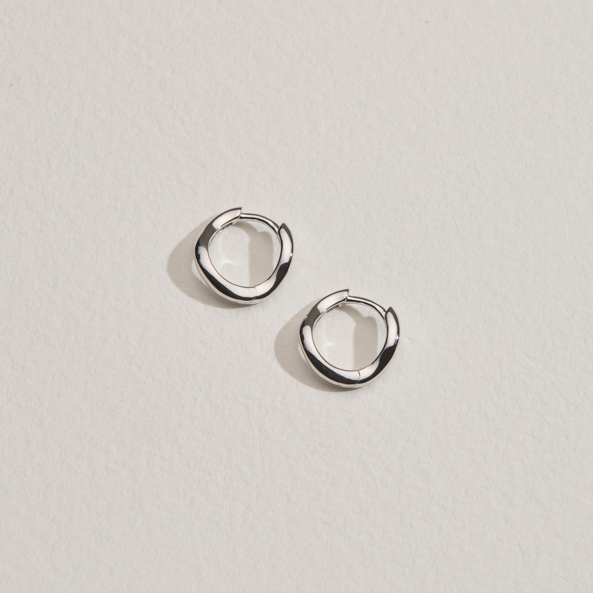 Silver wave huggie hoop earrings on a paper surface