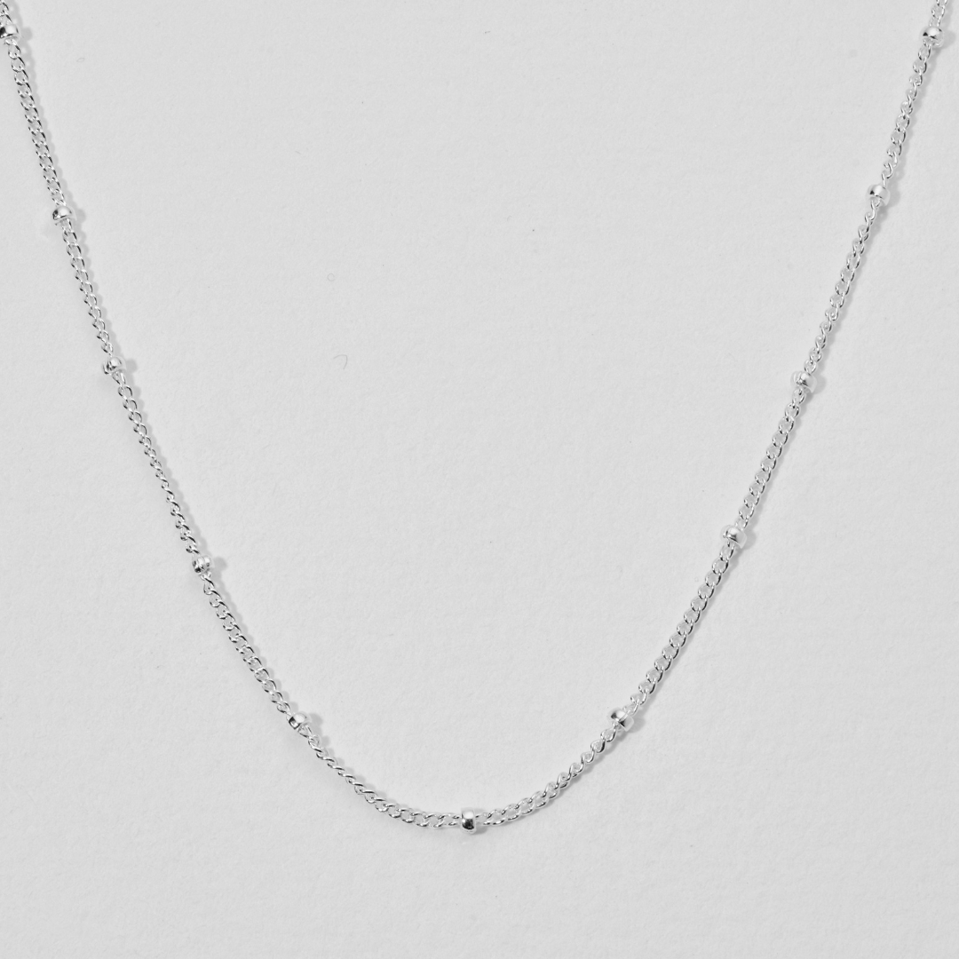 Close up of silver satellite chain necklace on a white background