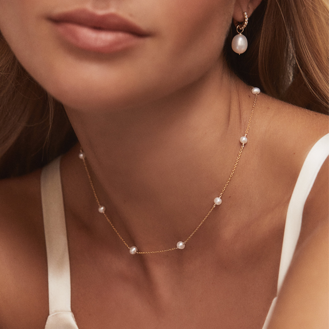 Gold ten pearl choker around a neck paired with a gold huggie pearl drop earring in one ear