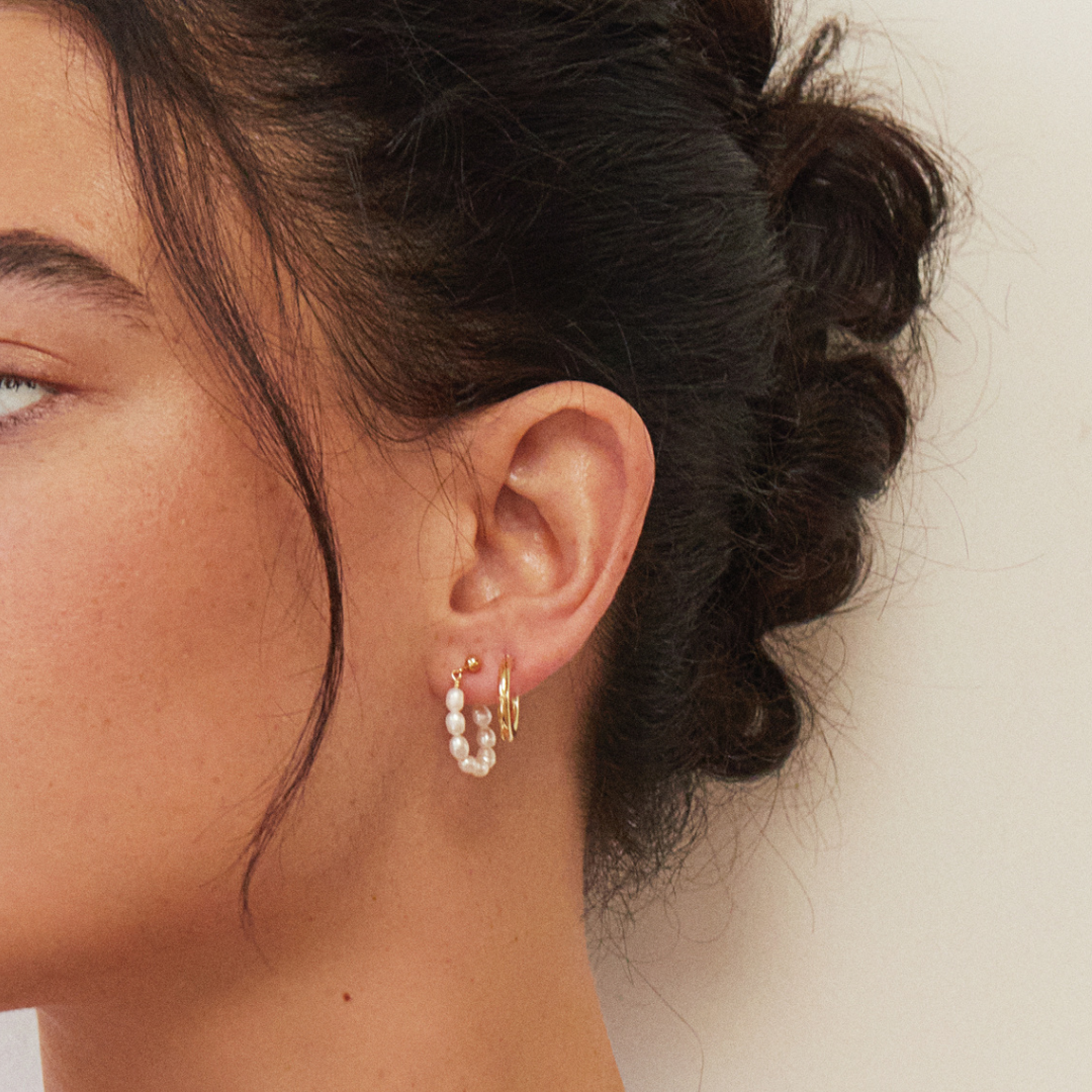 Gold seed pearl hoop earring and a gold hoop earring in a brunette woman's ear lobe