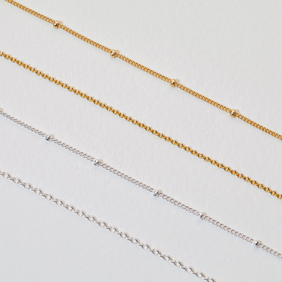 Silver satellite chain necklace, gold satellite chain necklace, gold chain necklace and silver chain necklace on a white surface
