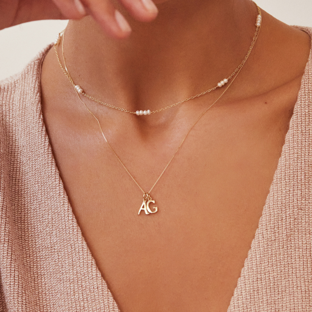 A gold mini pearl choker around a neck layered with a gold necklace with silver individual curve initial charms 'A' and 'G' on it 