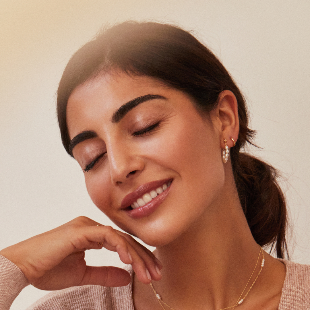 Gold seed pearl hoop earring and a gold huggie hoop earring in a woman's ear lobe also wearing a gold mini pearl choker around her neck