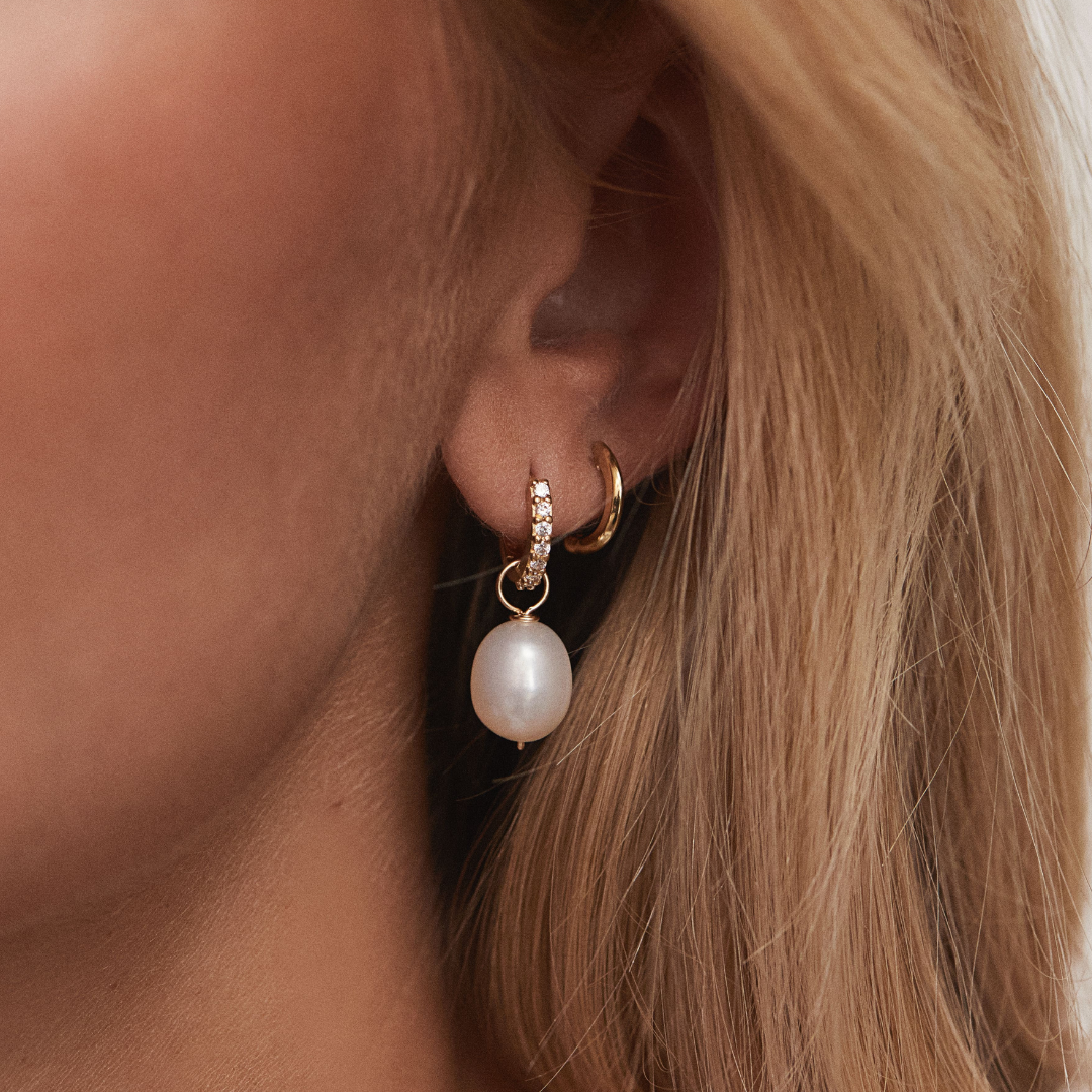 Gold huggie pearl drop earring and gold cuff in one ear lobe of a blonde woman
