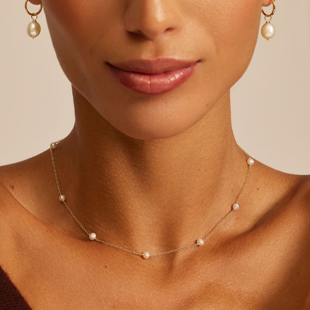Close-up of a woman wearing a pearl choker and earrings on a beige background