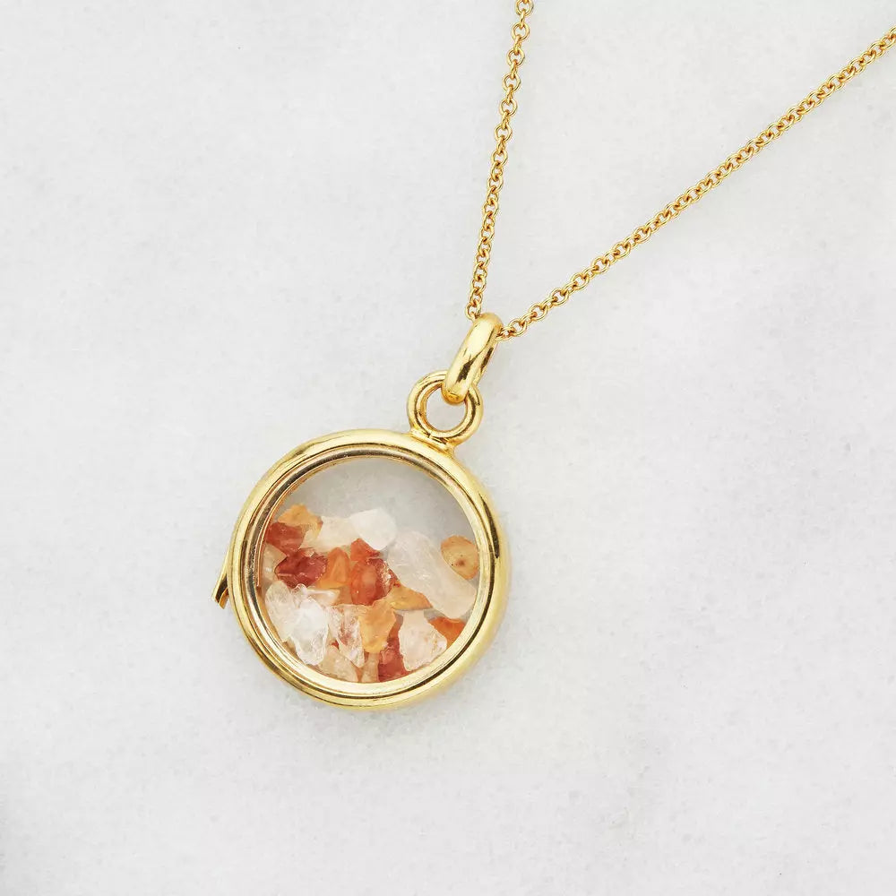 Gold glass gemstone locket with transparent white and red gemstones on a grey background