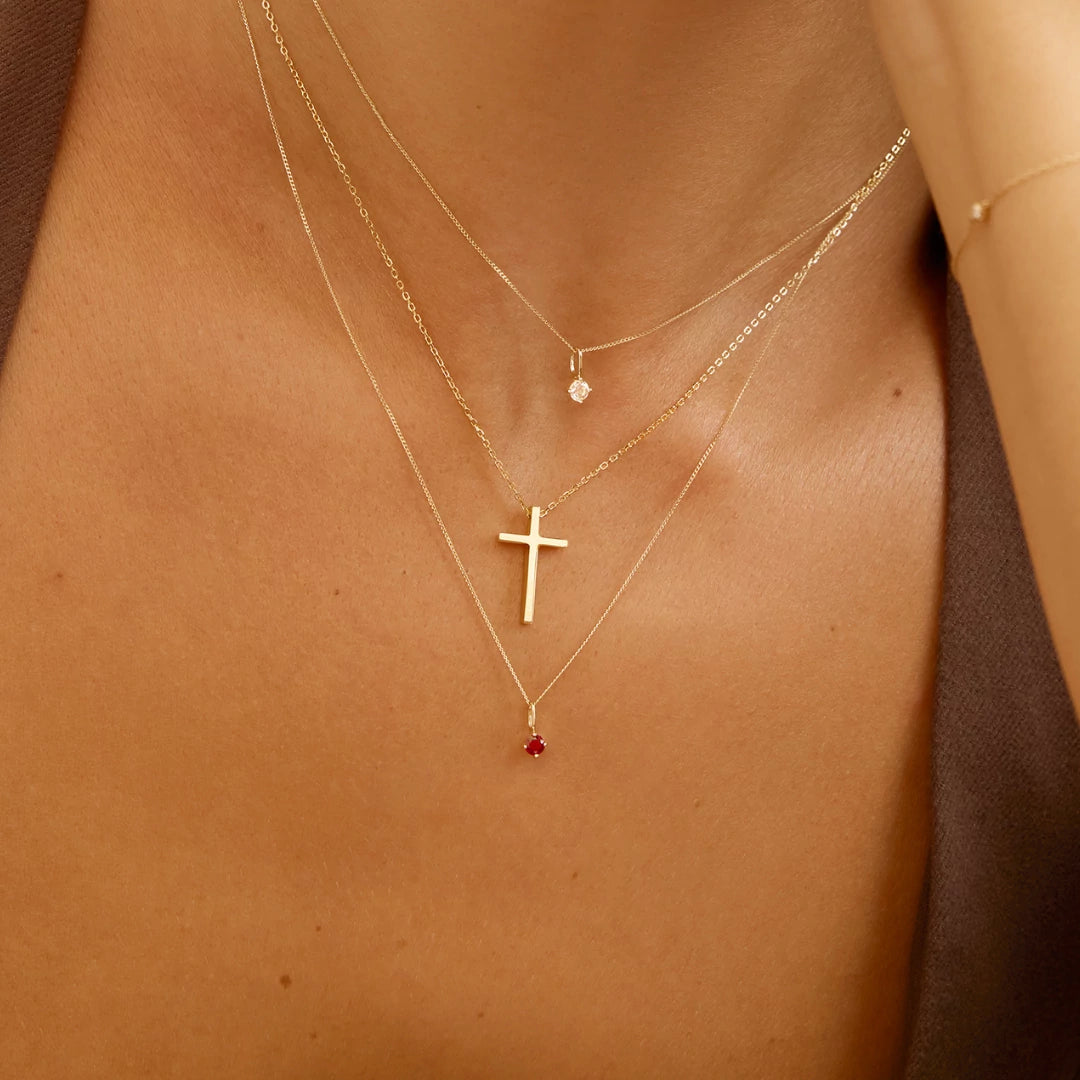 Close-up of a person wearing three gold necklaces with pendants on a neutral background