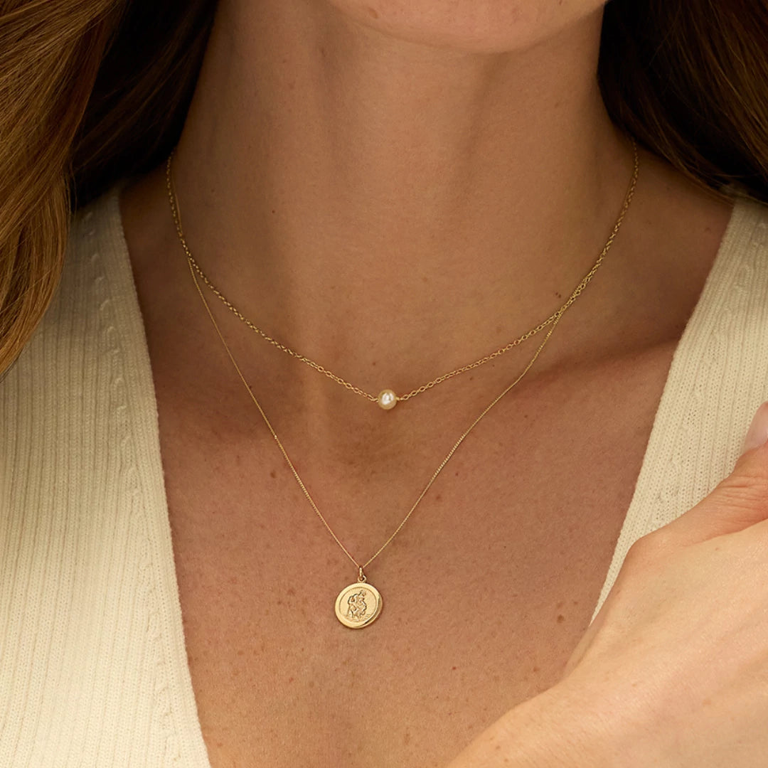 Close-up of a person wearing two gold necklaces. One with a pearl choker and the other a st christopher pendant.
