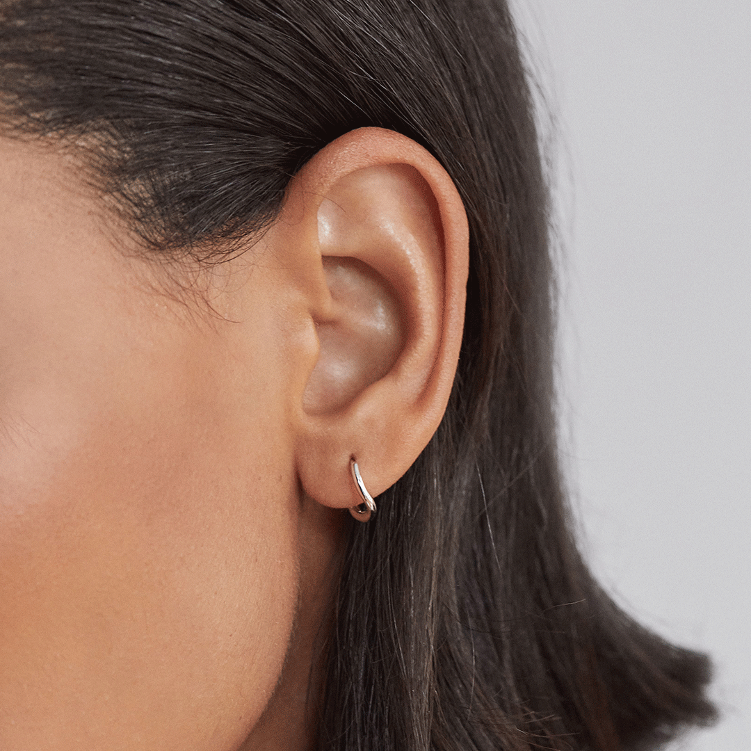 Silver wave huggie hoop earring in an ear lobe