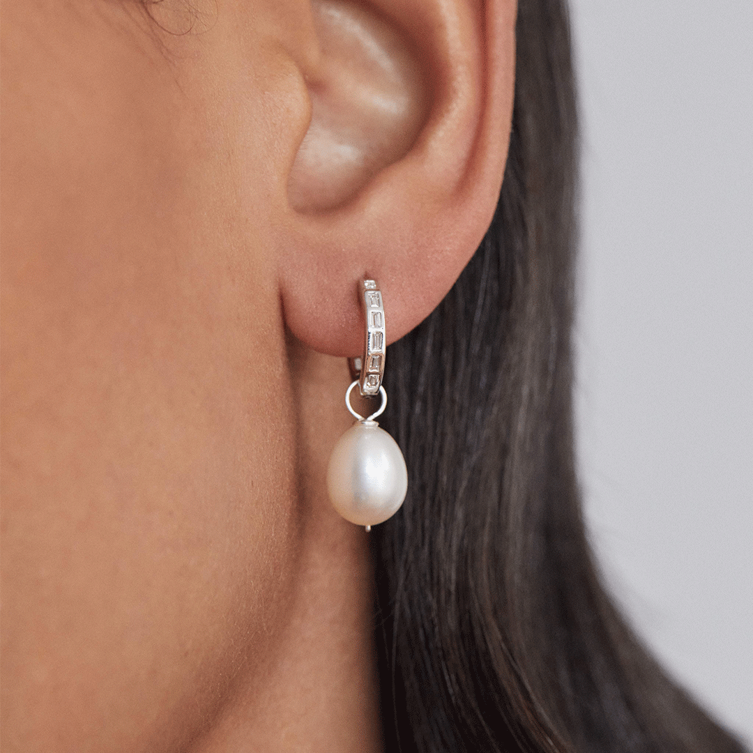 A silver diamond style baguette medium hoop earring in one ear lobe close up