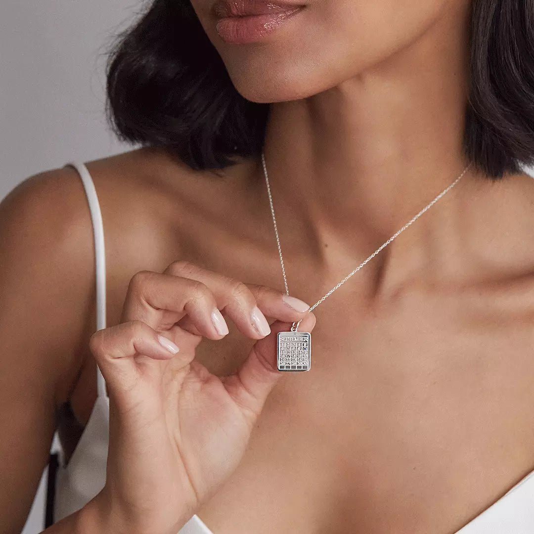 Silver special date calendar necklace 'September' with a gemstone on number '10' around the neck of a woman holding it up with her hand