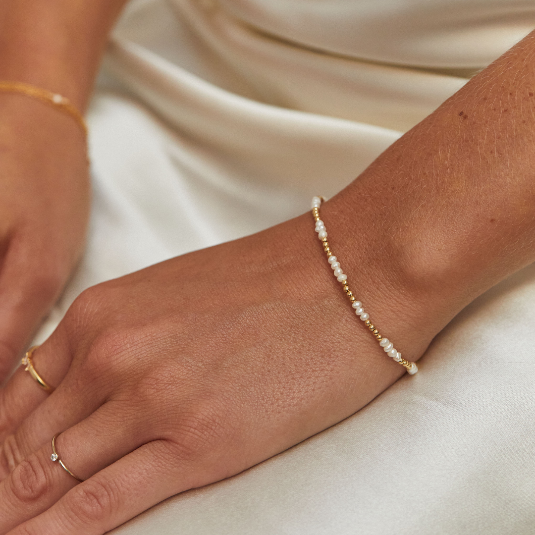 Gold beaded mini pearl bracelet on wrist with rings on fingers