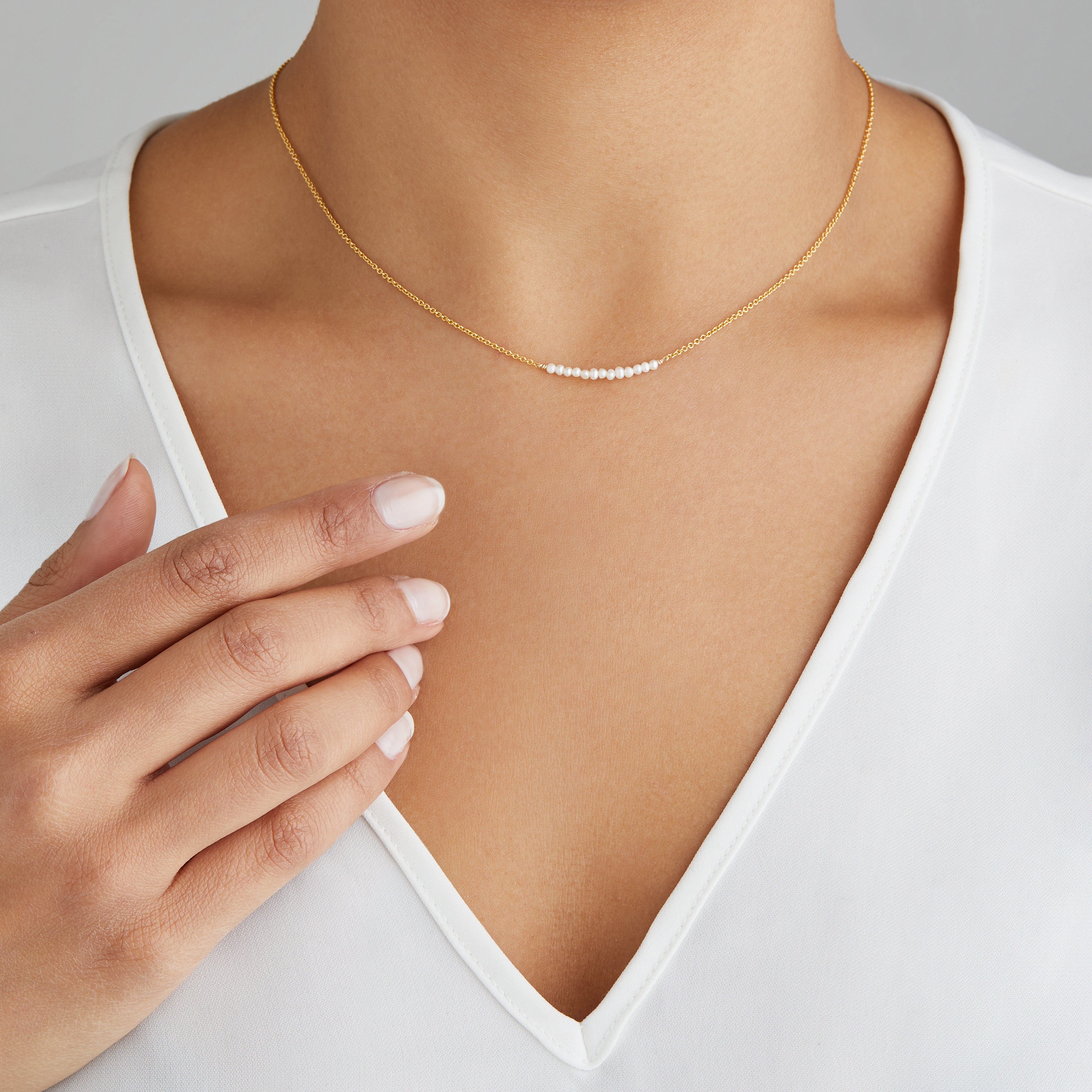 Gold small pearl cluster choker around a neck with a white V neck top