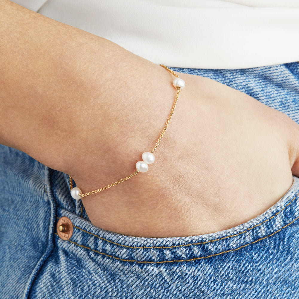 Gold six pearl bracelet around the wrist of a woman with her hand in a blue denim pocket