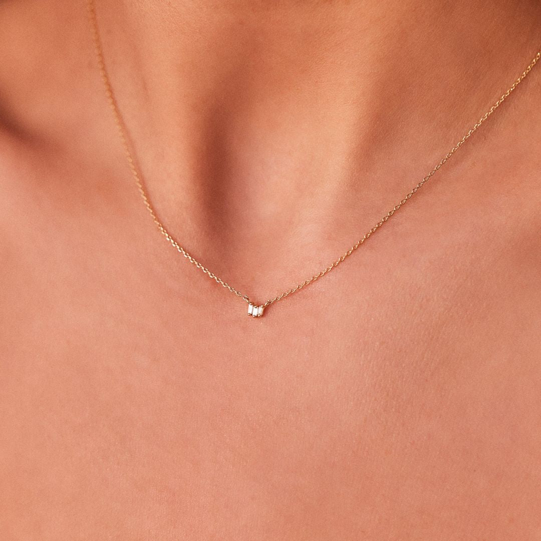 Silver triple baguette diamond necklace around a neck close up