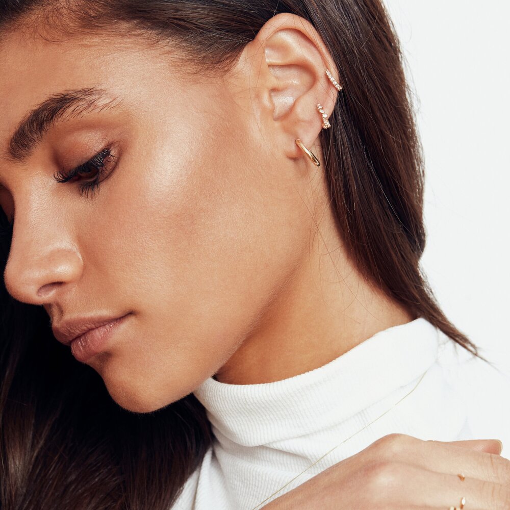 A gold diamond style jagged huggie hoop earring and a gold diamond style cluster huggie hoop earring and a plain gold huggie hoop earring in one ear lobe