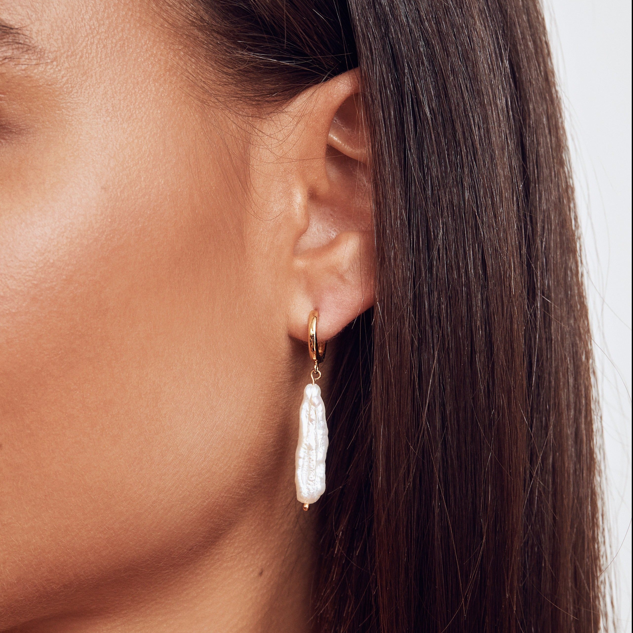 Gold baroque pearl shard hoop earring in one ear lobe close up
