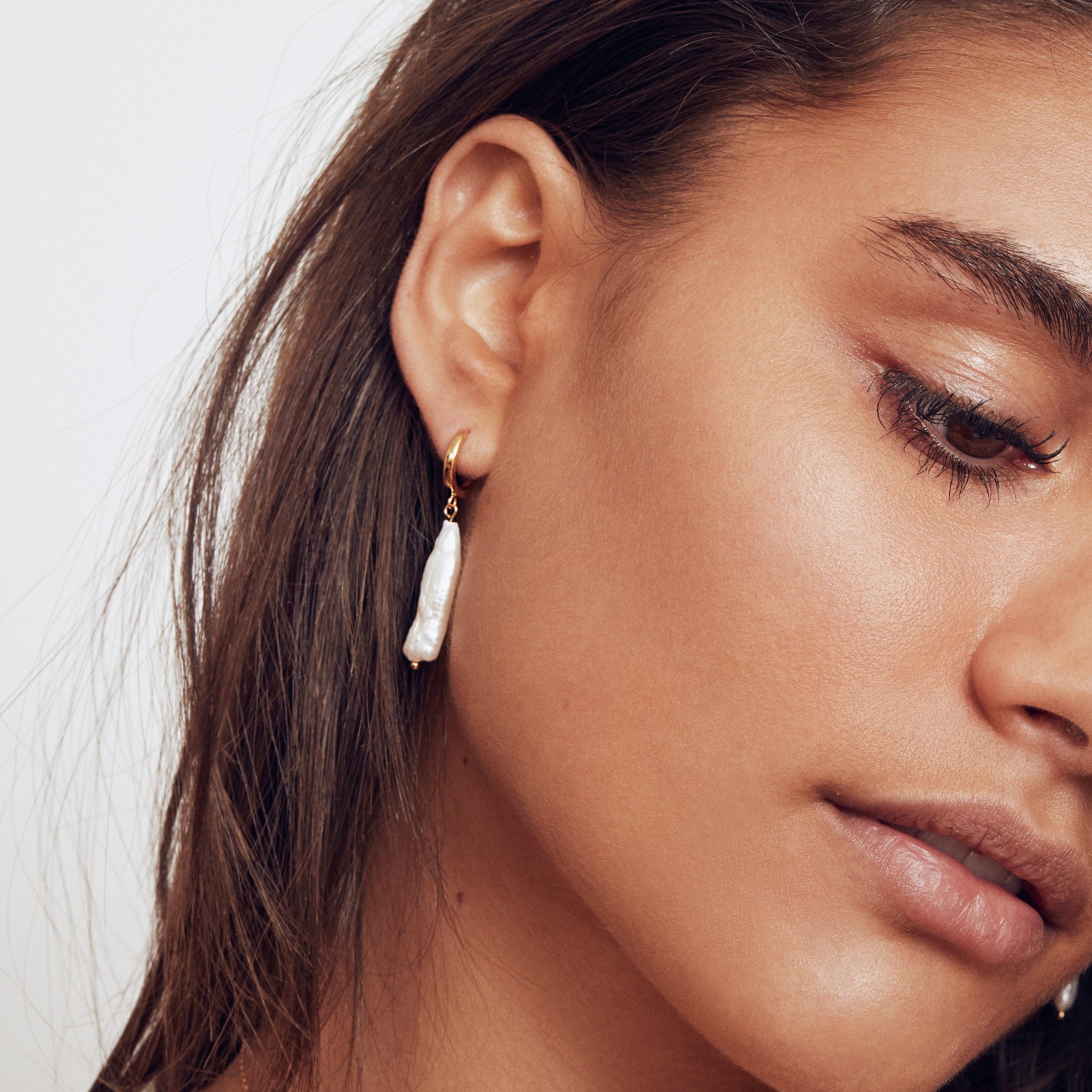 Silver baroque pearl shard hoop earring in one ear lobe with her hair tucked behind her ear