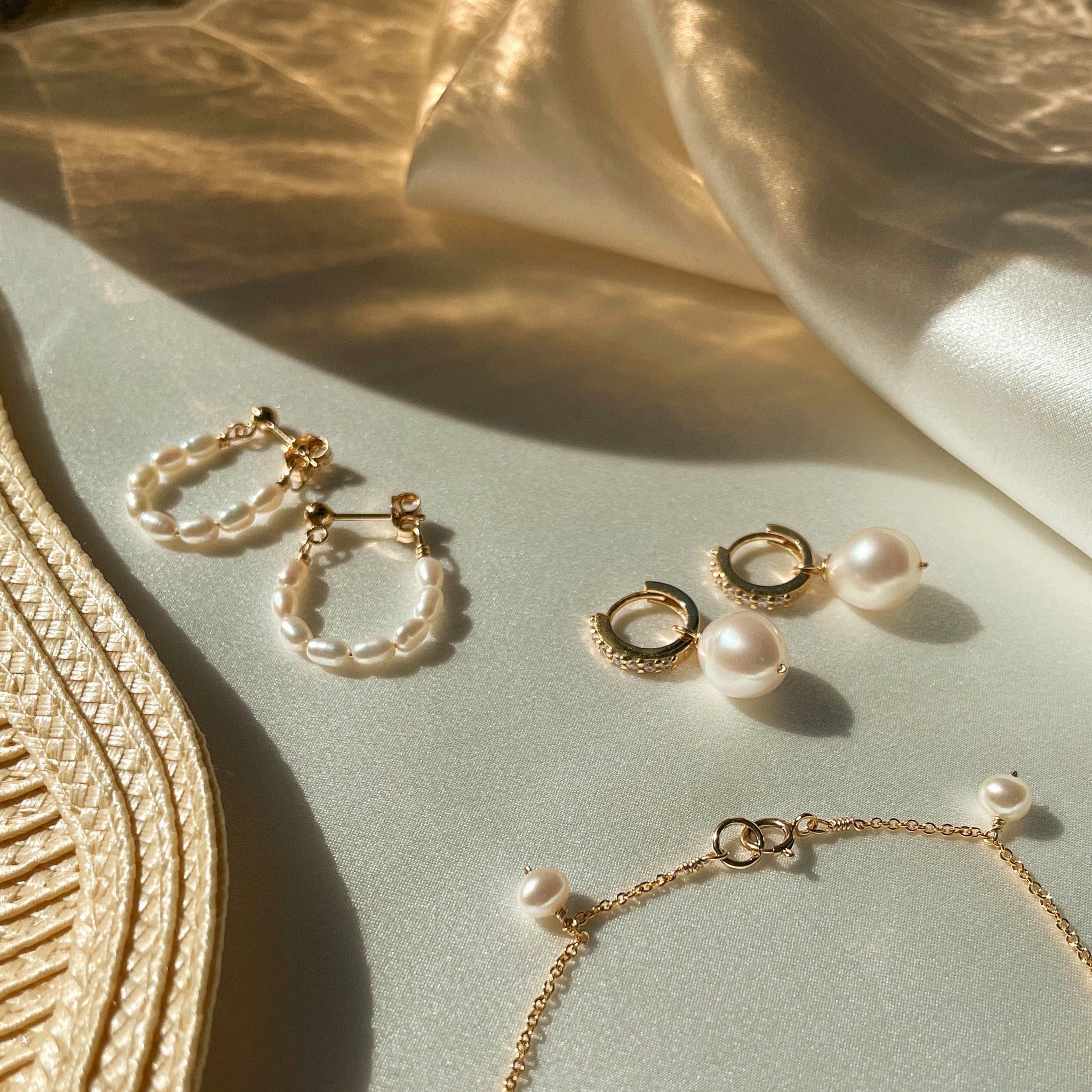 Gold seed pearl hoop earrings and other pearl earrings on shiny white silk surface