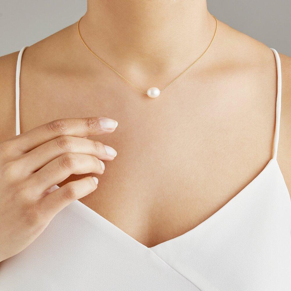 Gold large single pearl choker around neck with a white top