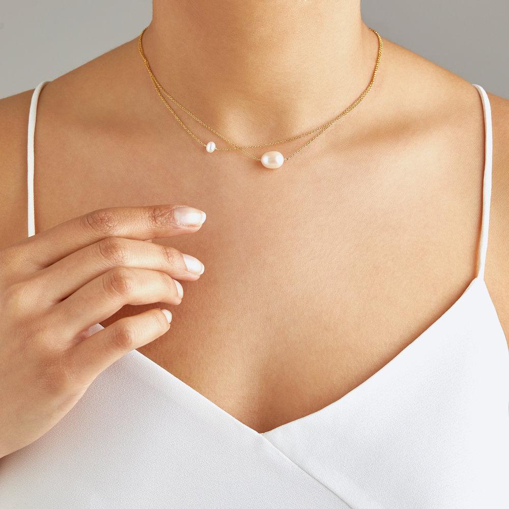 Gold layered large and small pearl choker around a neck with a white top