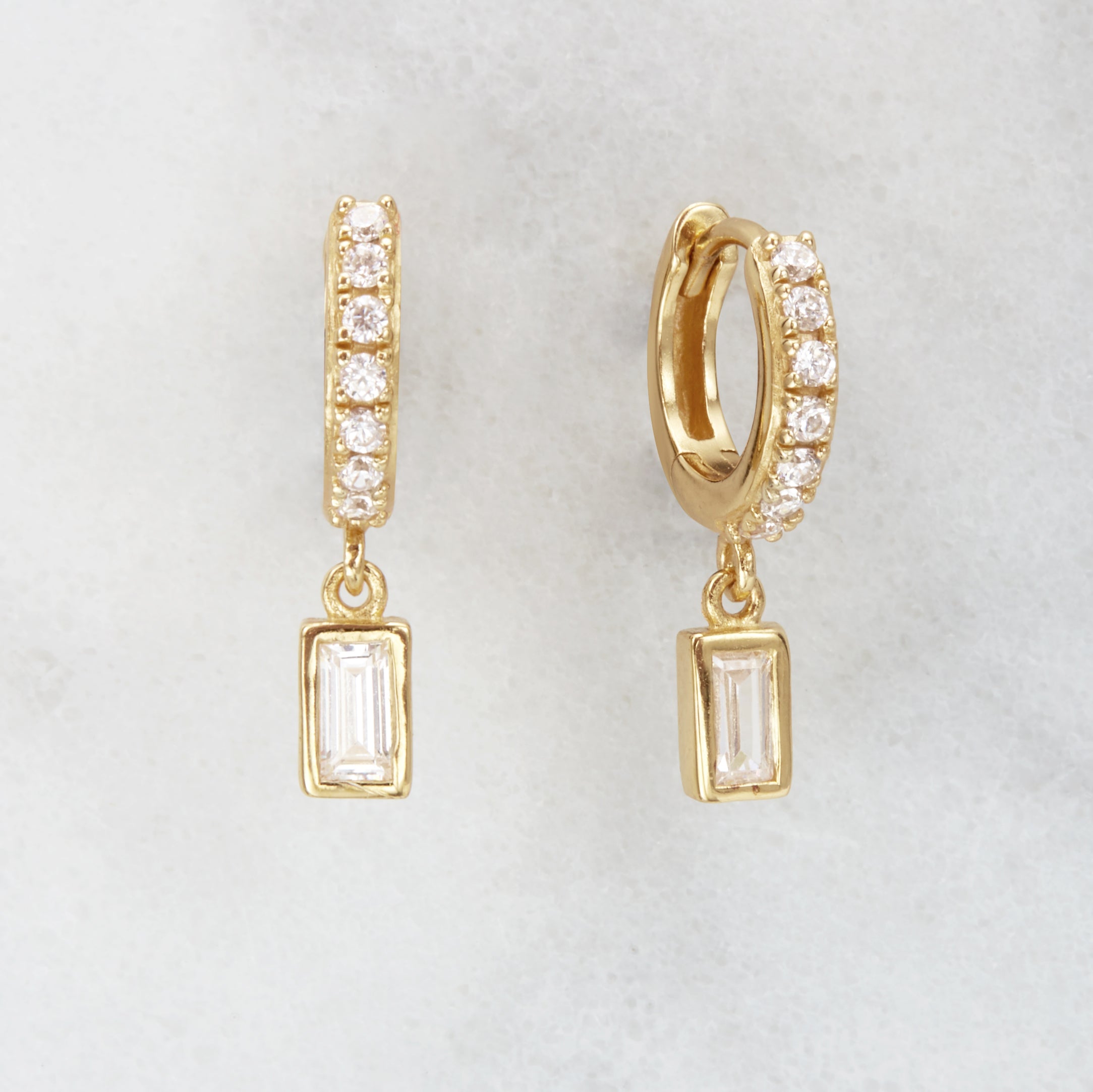 Gold diamond style baguette drop huggie hoop earrings on a marble background
