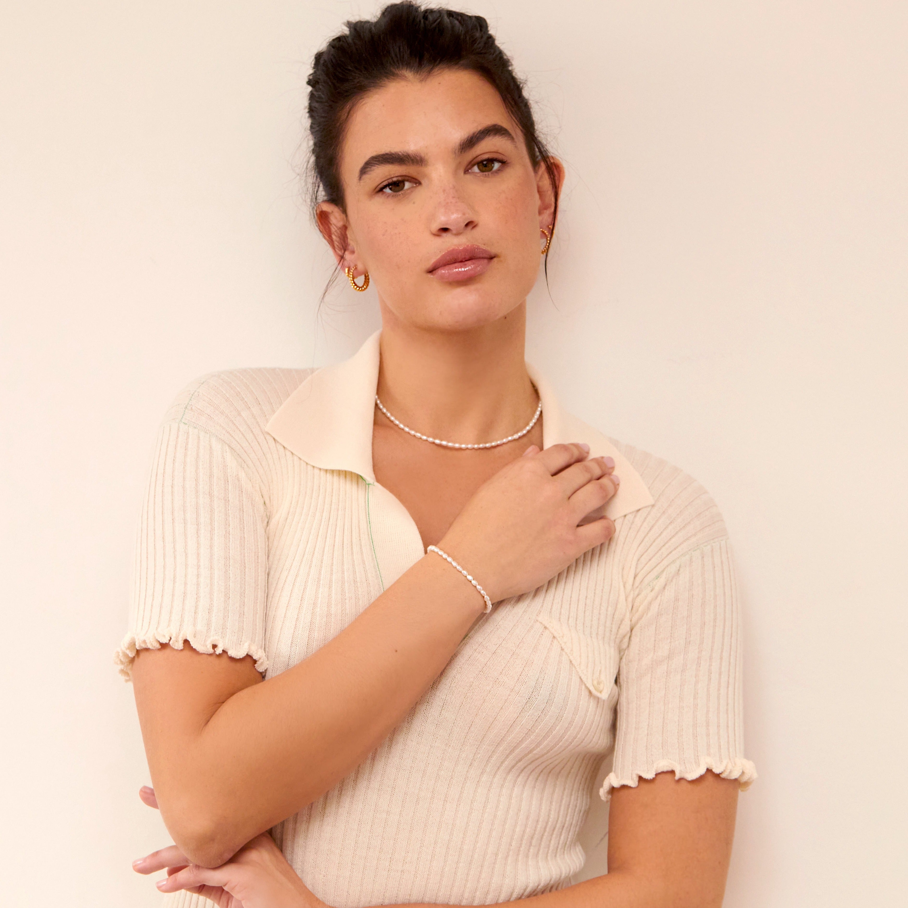 Woman wearing a gold seed pearl bracelet on her wrist and matching gold seed pearl choker around her neck, her arm placed across her chest to display the bracelet