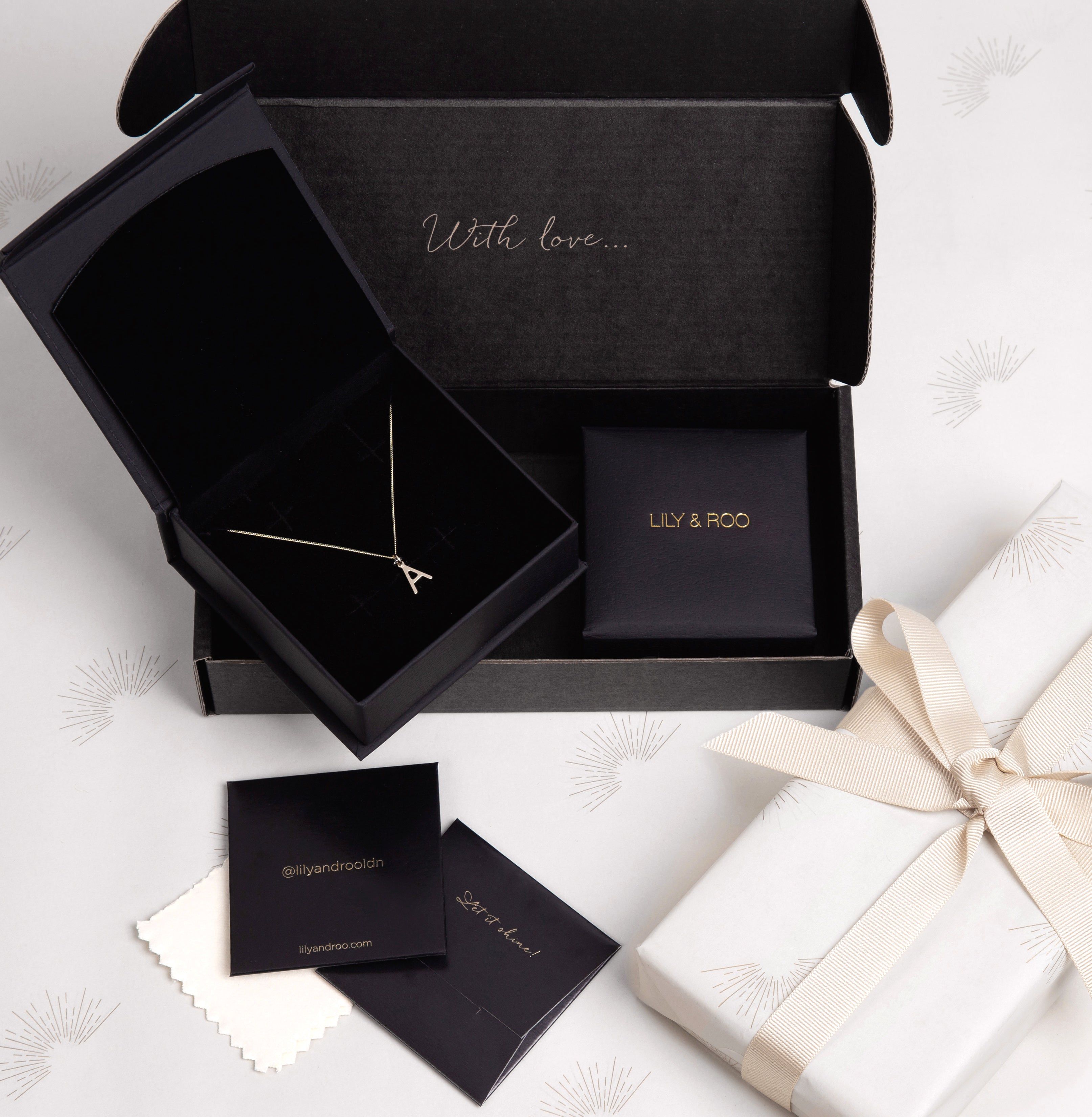 A necklace inside a black gift box alongside other gift boxes