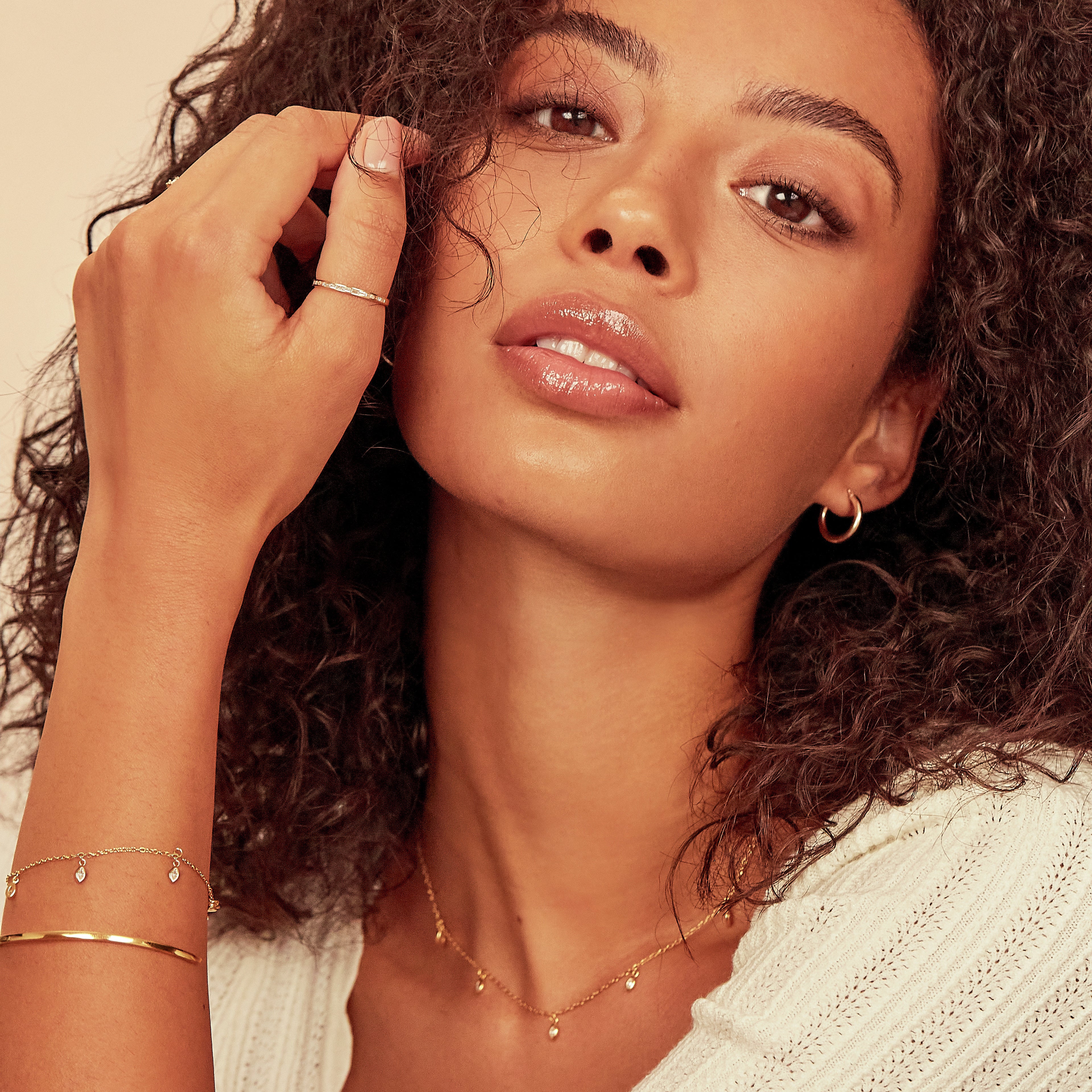 A gold thin engraved bangle layered with a gold diamond style marquise drop bracelet on a woman's arm with a gold diamond style marquise drop necklace around her neck and a gold diamond style baguette eternity ring on her finger and a gold hoop earring in one ear lobe