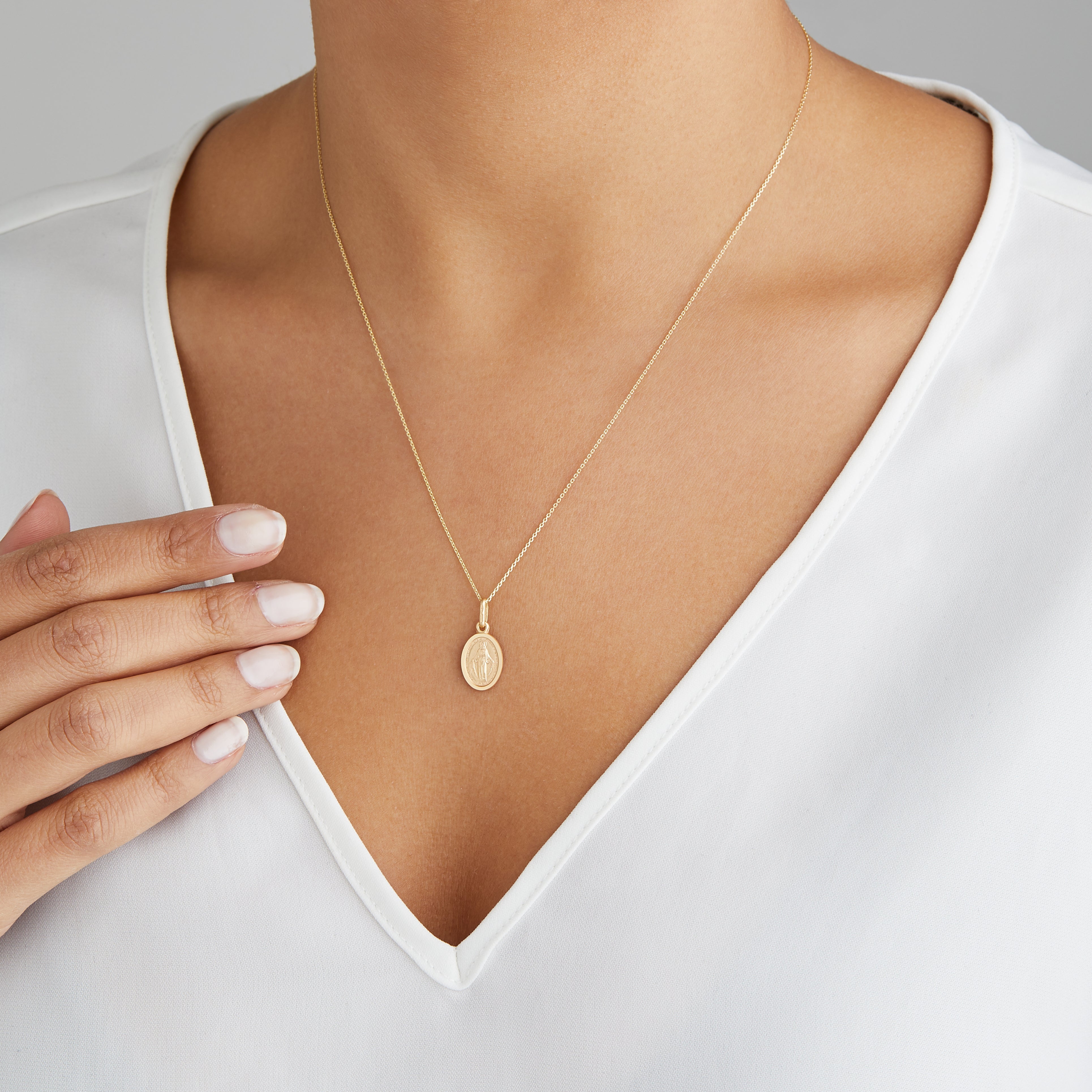 Gold small virgin mary necklace around the neck of a woman wearing a white V-neck top