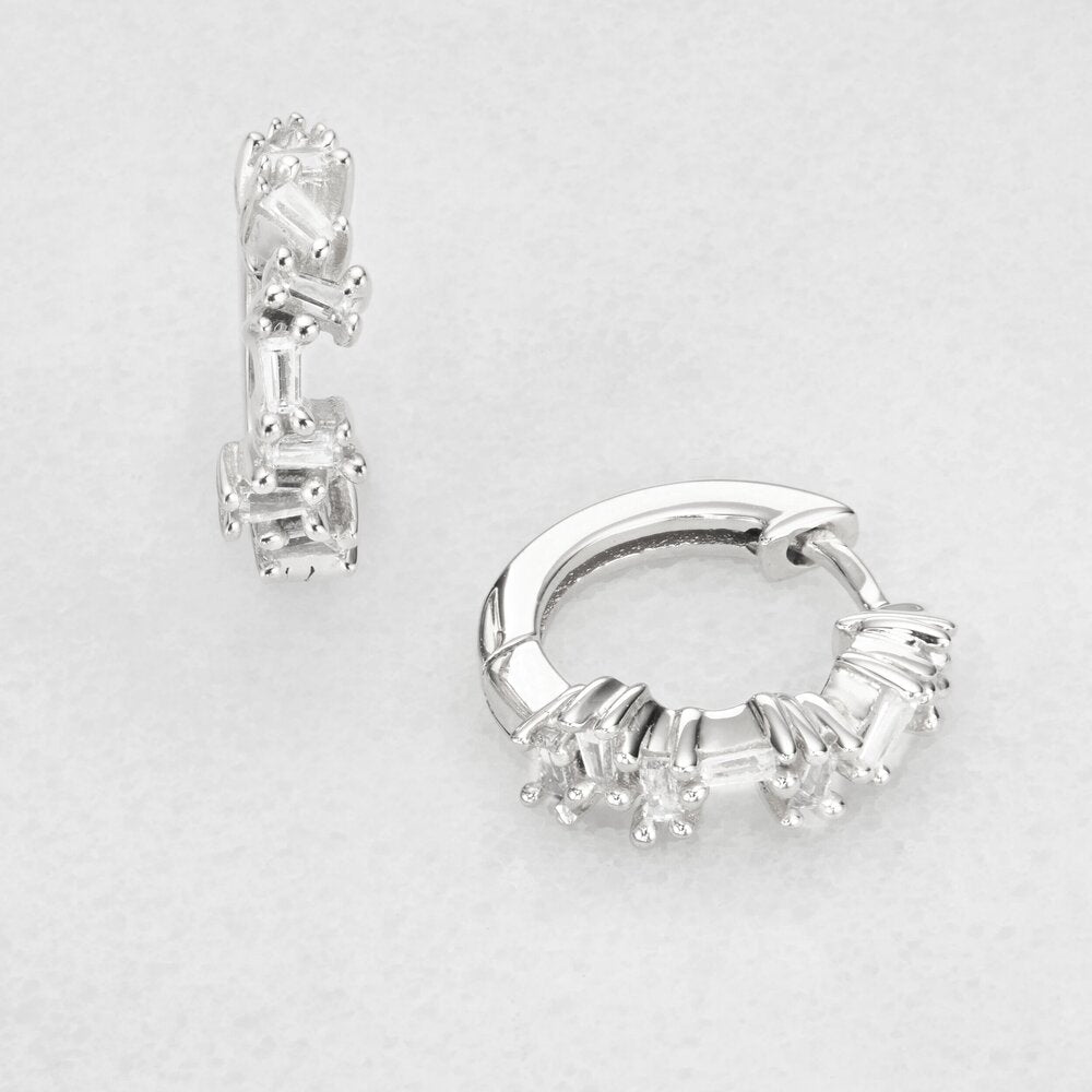 Silver diamond style jagged huggie hoop earrings on a marble surface