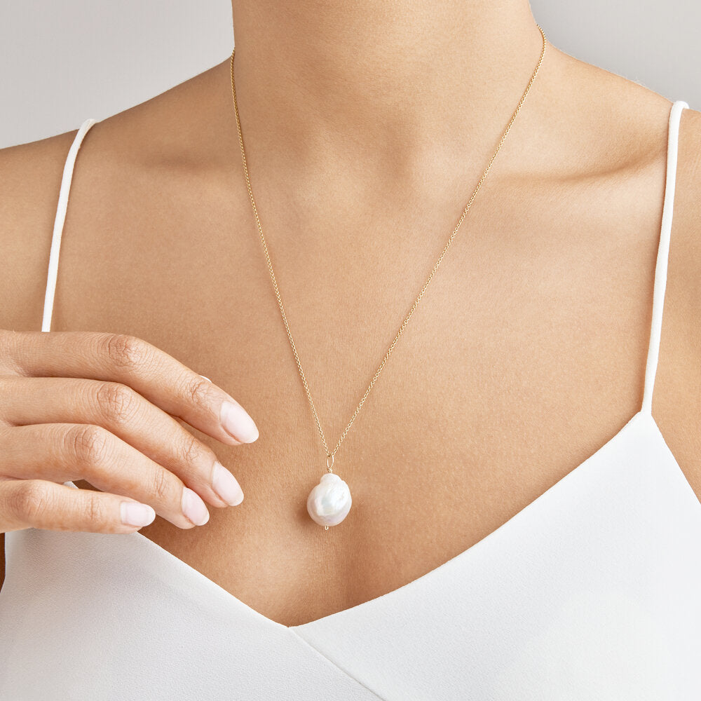 Gold extra large baroque pearl necklace around neck with a white top