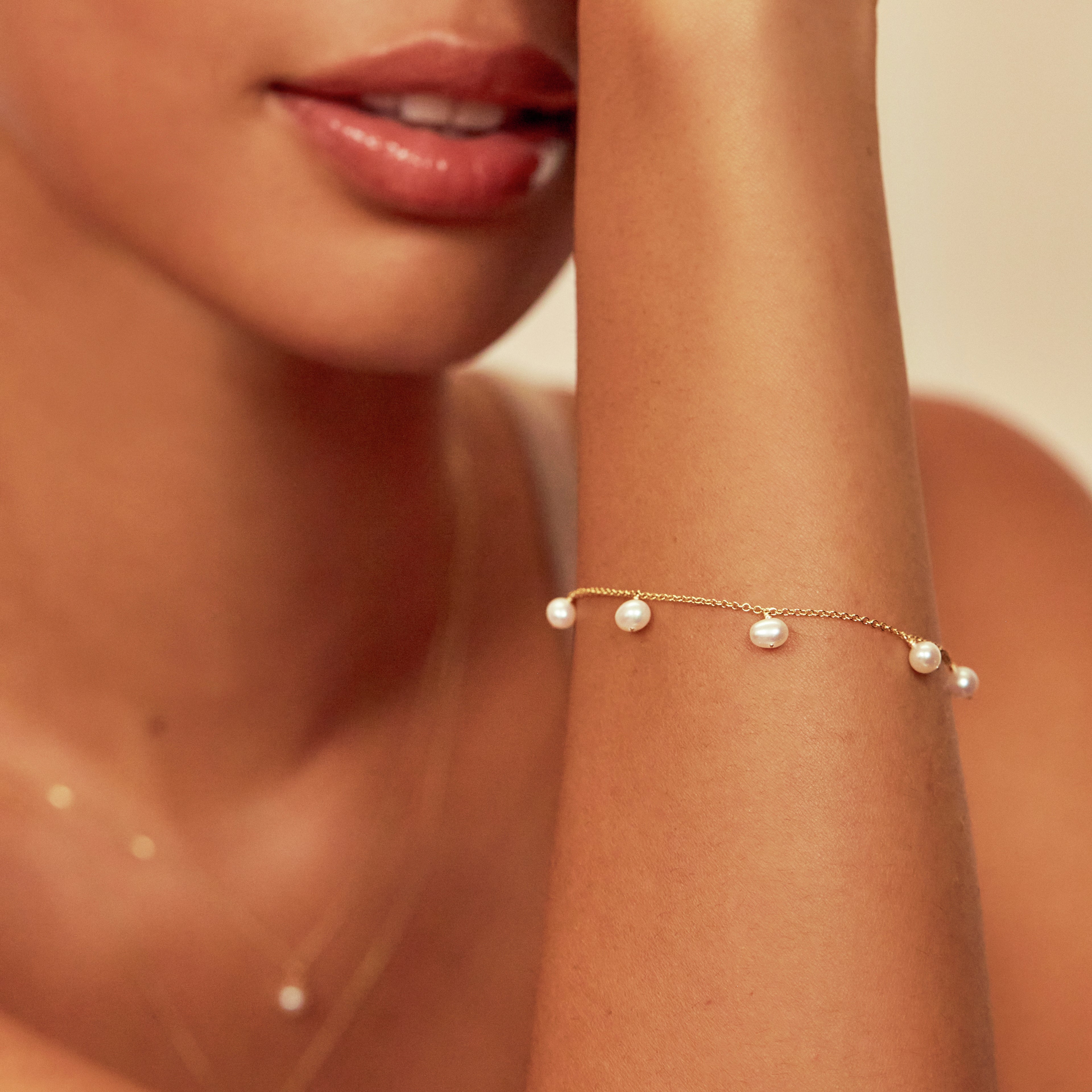 Gold pearl drop bracelet around a wrist held up close to her face 