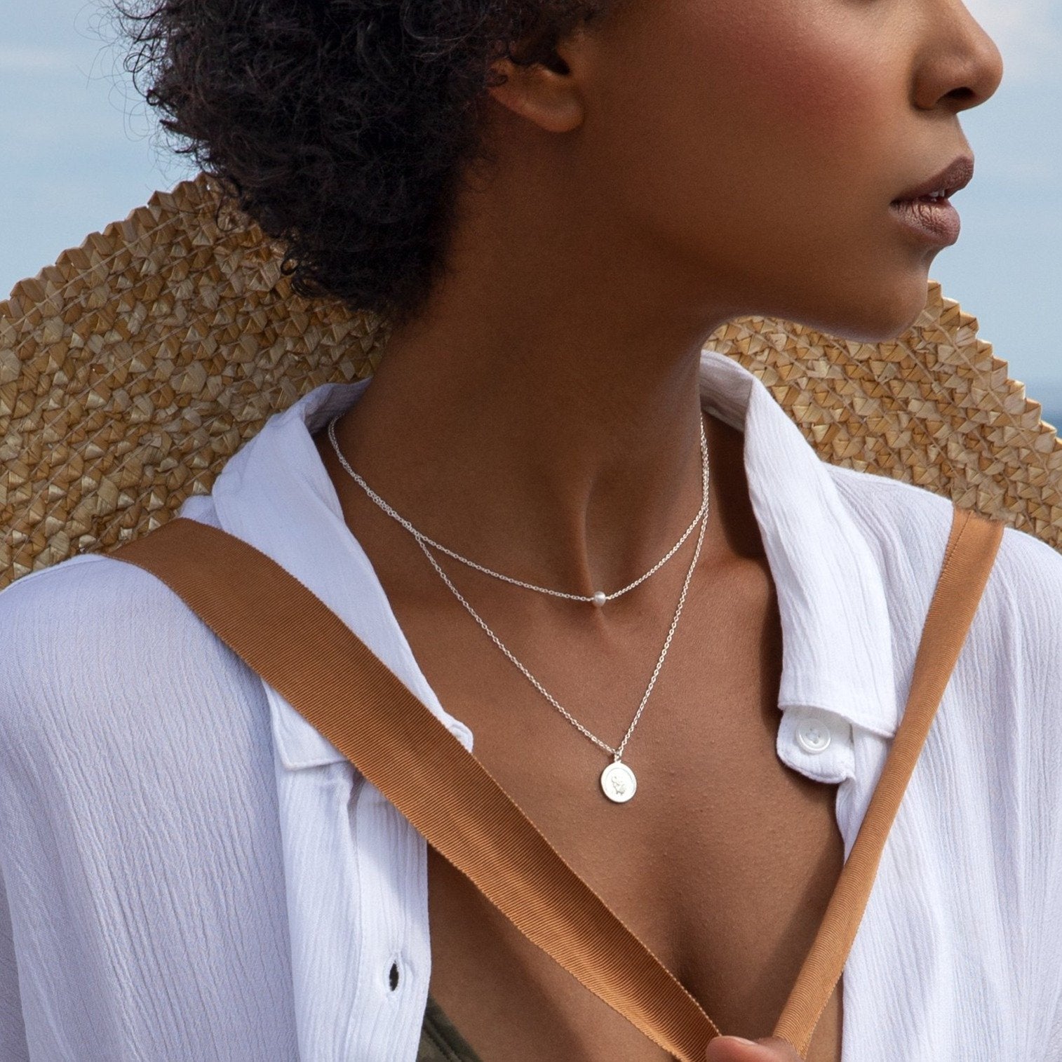 Woman in a white shirt wearing a silver single pearl choker layered with a silver symbol necklace around her neck