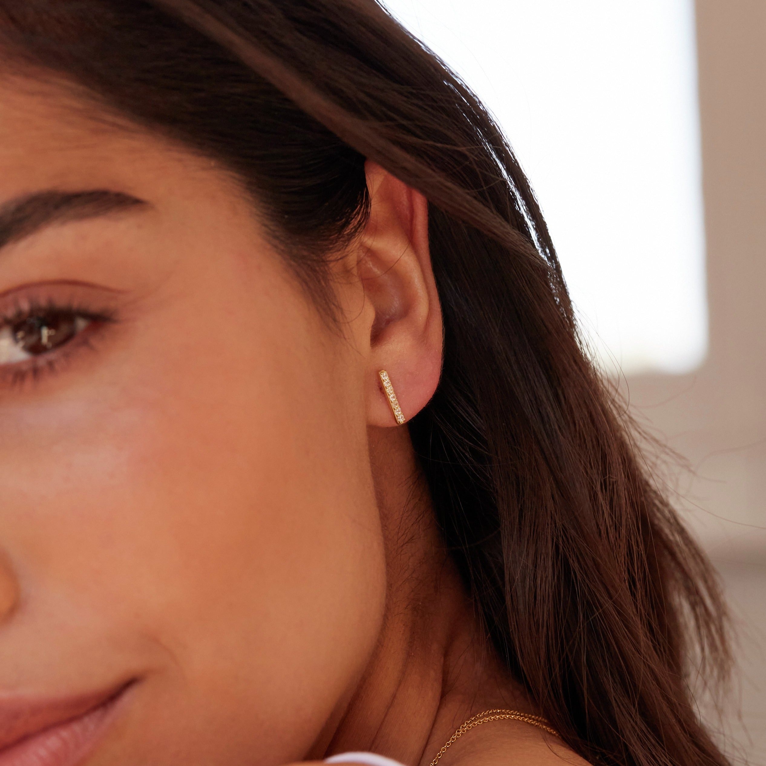 Gold diamond style bar stud earring in one ear lobe on a brunette woman